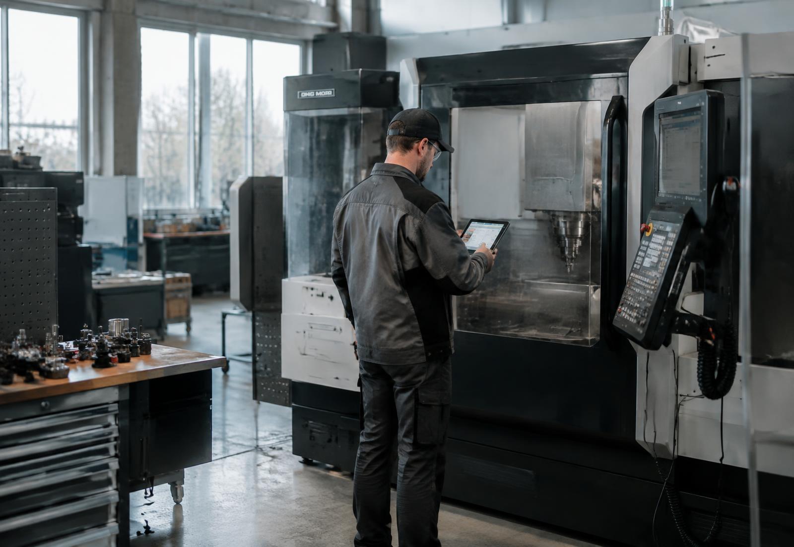 Medarbejder ved CNC-maskine med tablet i produktionen